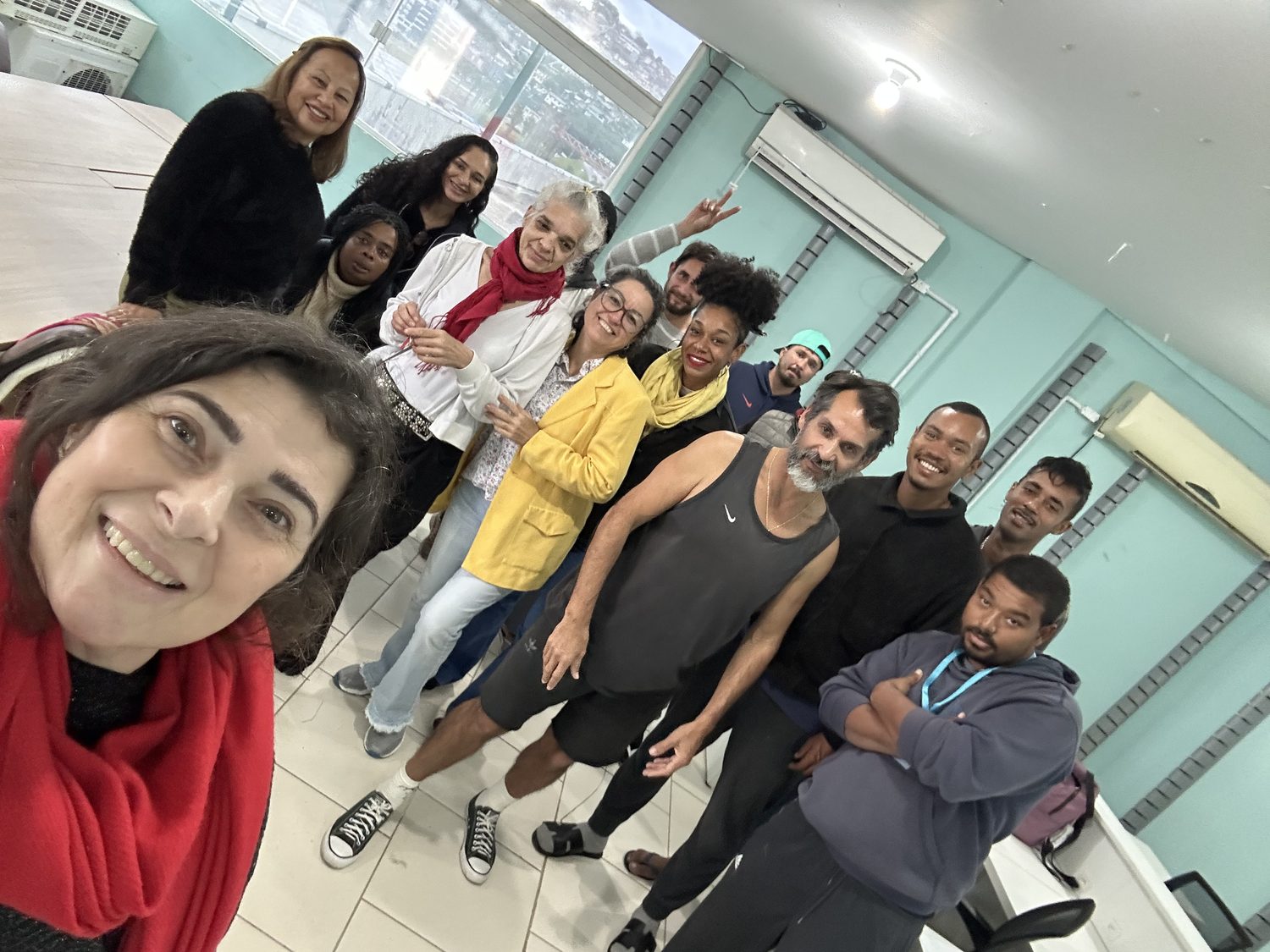 Participante sorrindo durante uma oficina, com a turma ao fundo na sala com vista para o mar